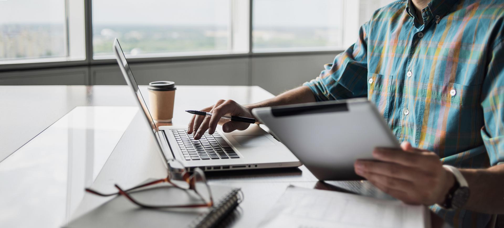 Man working on laptop computer and tablet in office, banner