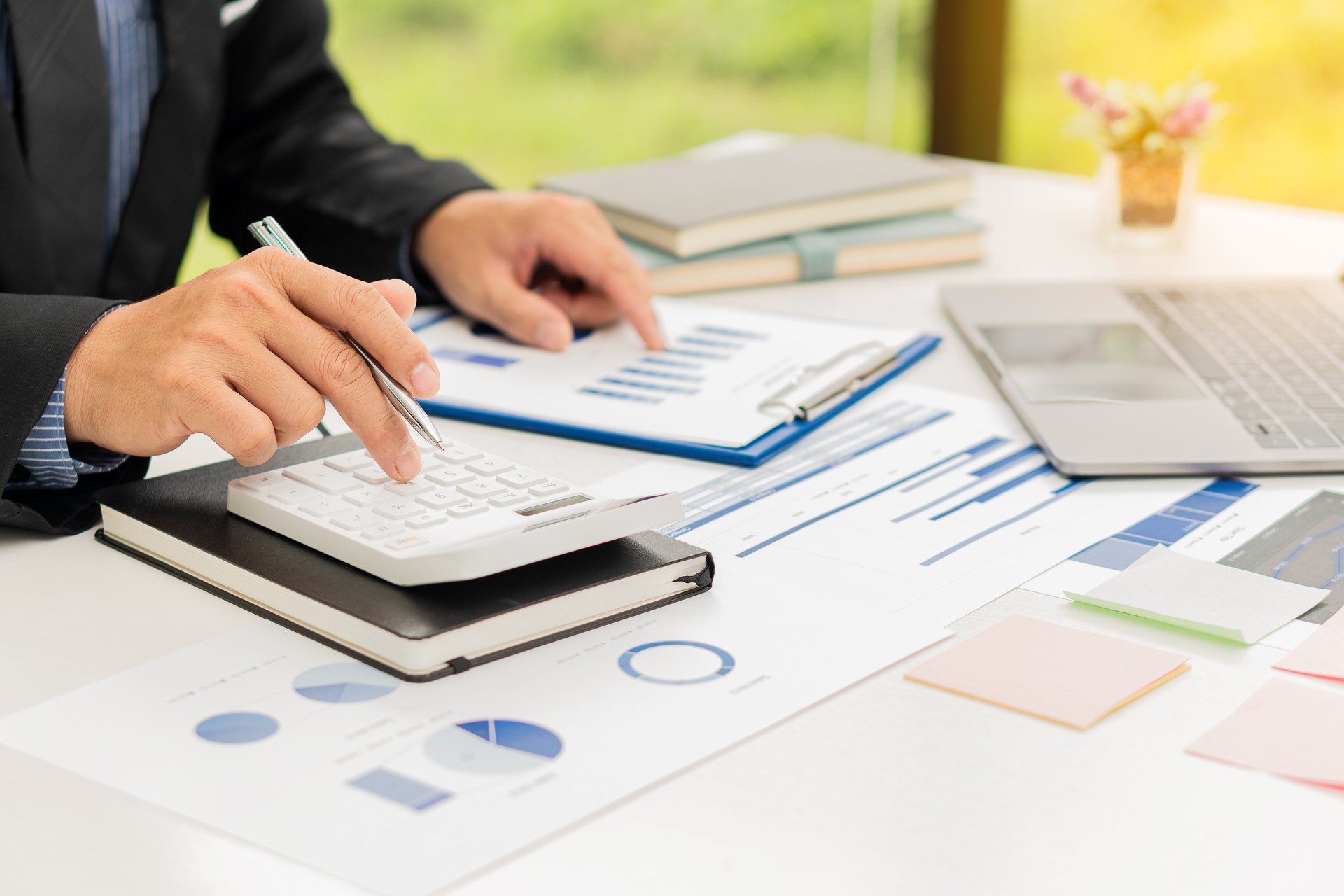 A businessman or accountant holds a pen and presses a calculator to calculate business information. Financial accounting graph document and notebook computer in the company office.